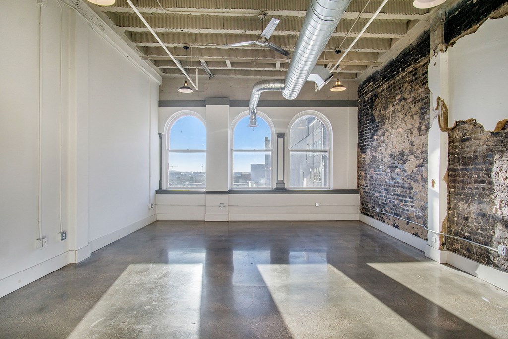 an empty room with three windows and a exposed brick wall