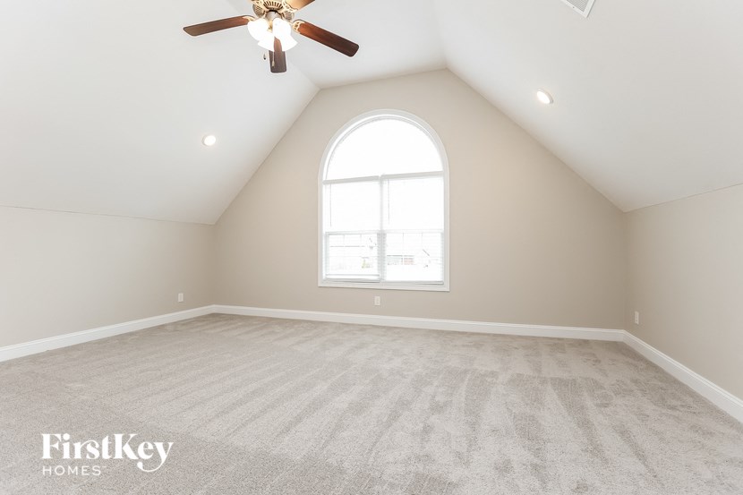 the loft of a home with an arched window and a ceiling fan