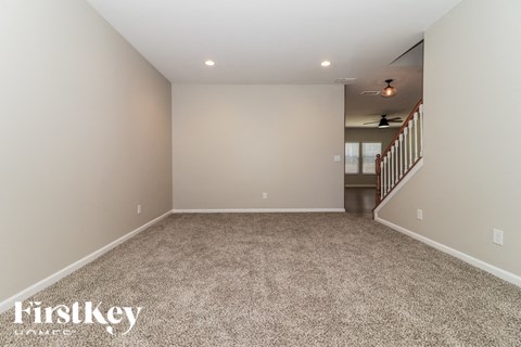 A spacious room with a carpeted floor and a staircase in the background.