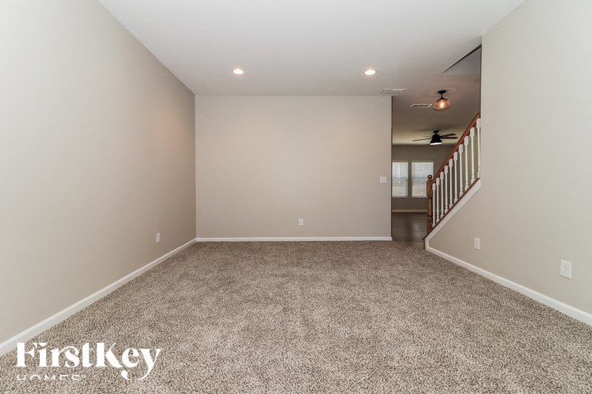 A spacious room with a carpeted floor and a staircase in the background.