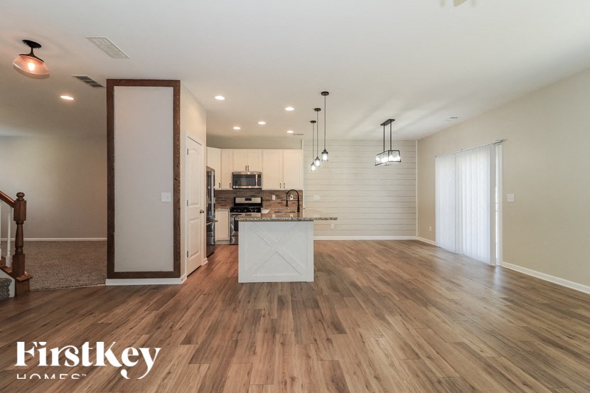 A spacious room with wooden floors and a kitchen area in the background.
