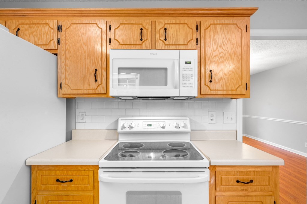 an empty kitchen with a stove and microwave and wooden cabinets