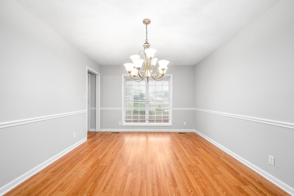 an empty living room with wood floors and a chandelier