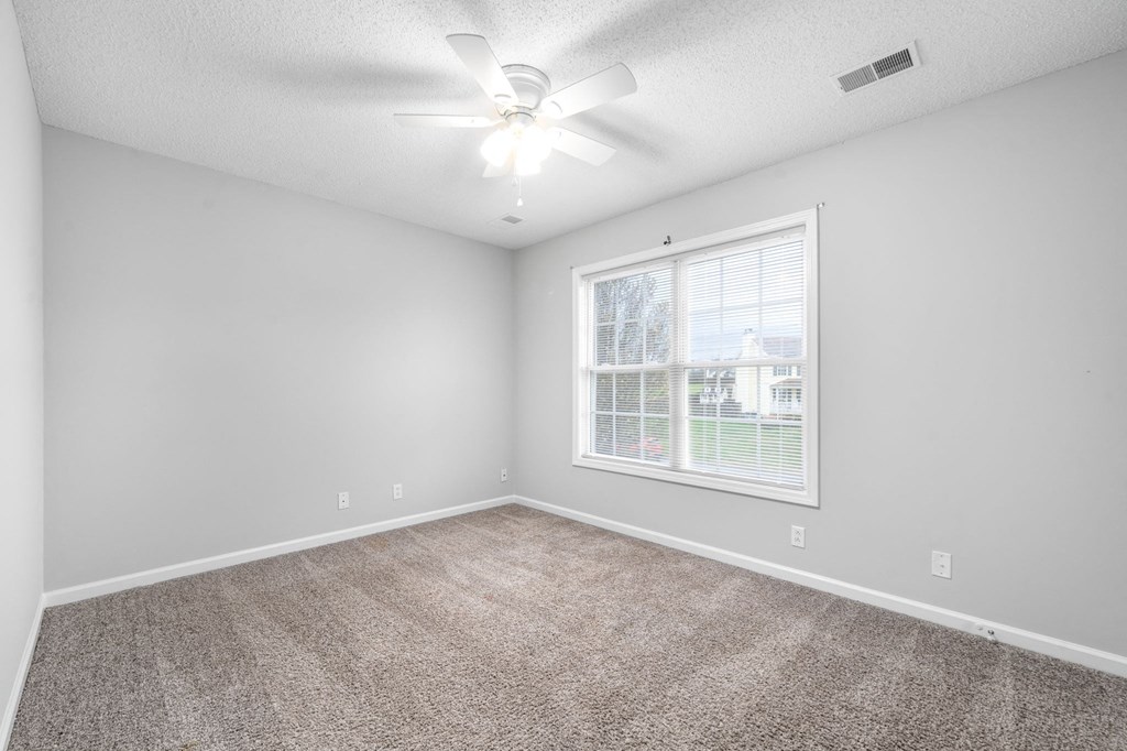 an empty living room with a large window and a ceiling fan