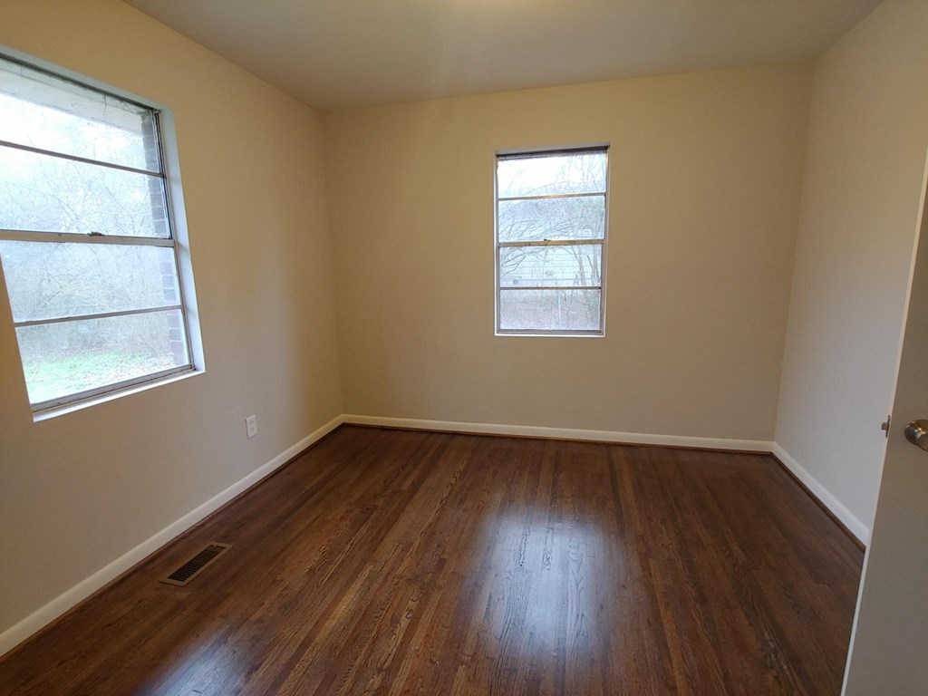 an empty room with wooden floors and two windows