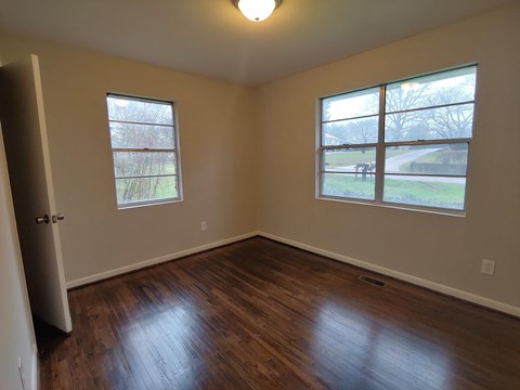 a bedroom with a hard wood floor and two windows