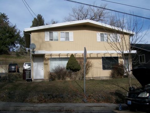 A beige house with a white door and a tree in front.