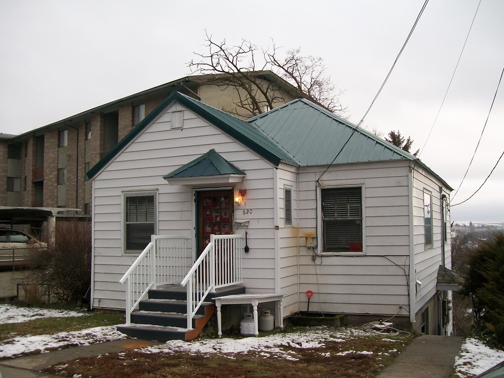 a small white church with a green roof and stairs in the snow