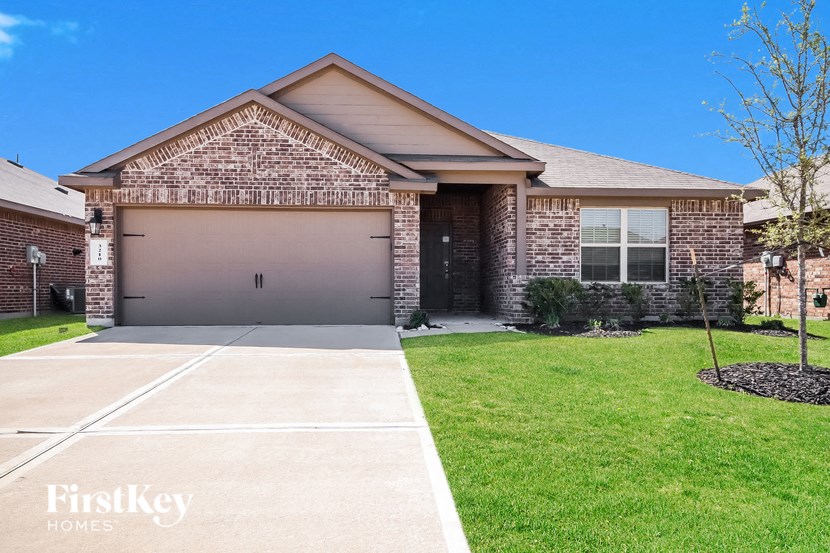 A brick house with a garage door and a tree in the front yard.