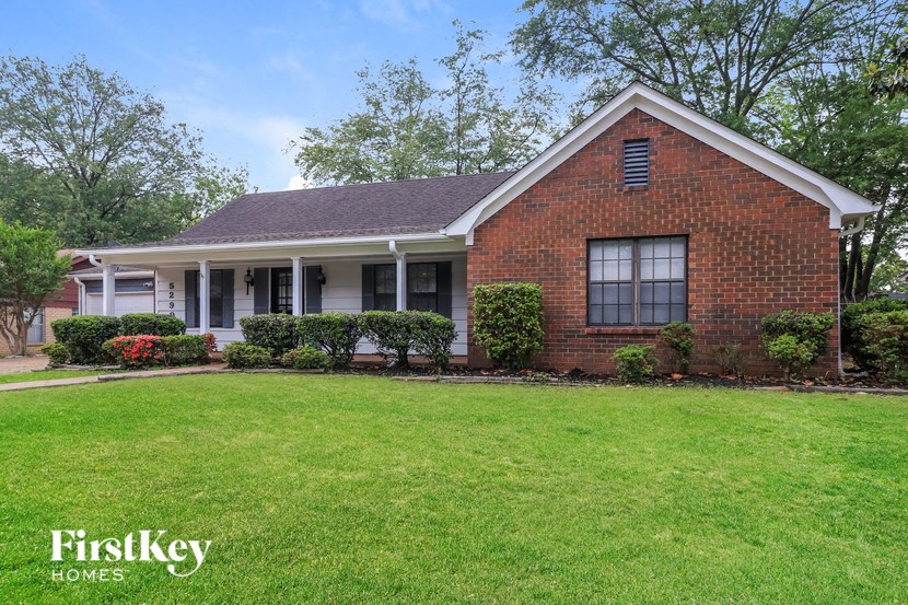 A brick house with a white porch and a green lawn in front.