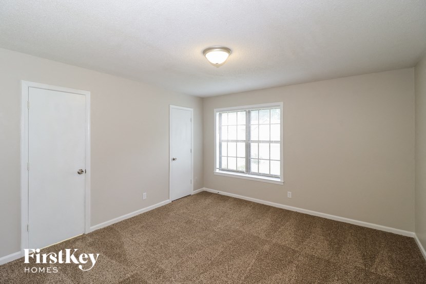 A room with a carpeted floor and a window with white blinds.