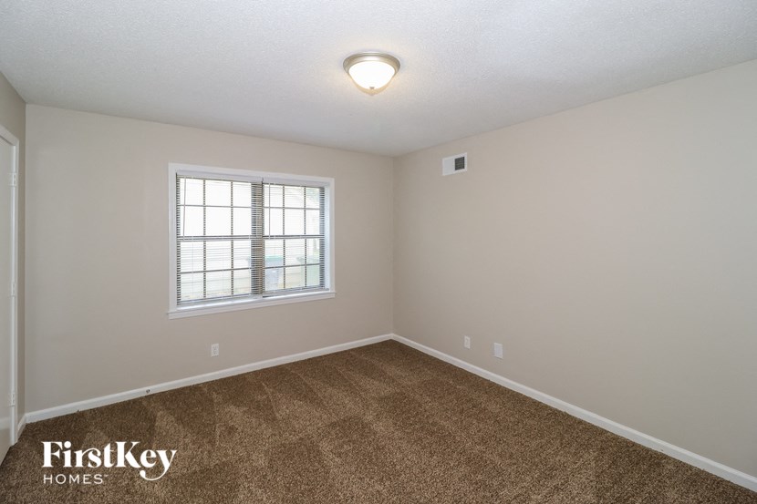 A room with a carpeted floor and a window with blinds.