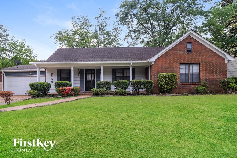 A brick house with a white porch and a green lawn in front.