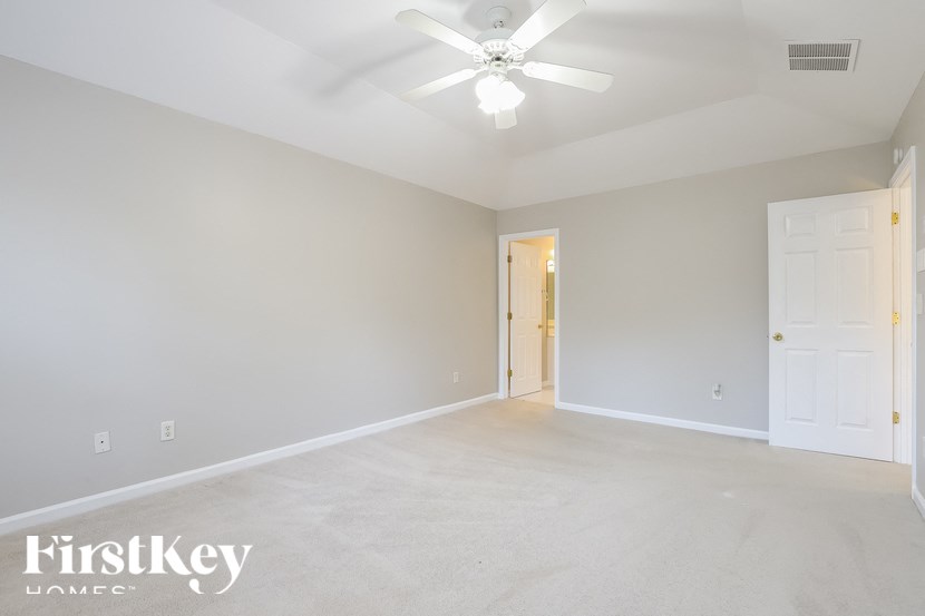 an empty living room with a ceiling fan and a door to a hallway