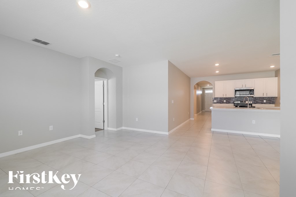 the spacious living room and kitchen with white cabinets and tile flooring