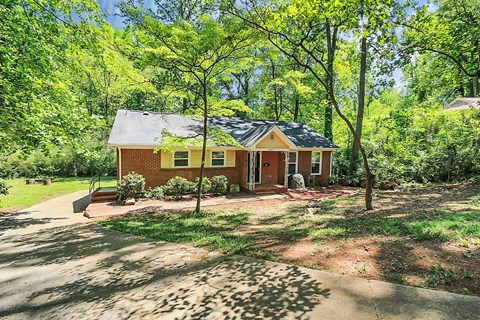 a small brick house with trees and a driveway