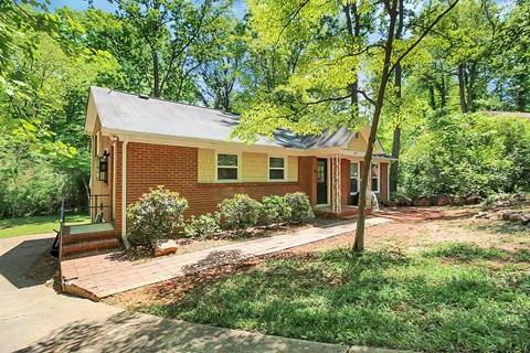 a small brick house with a porch and a yard with trees