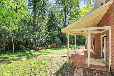 the front porch of a red brick house with a lawn and trees