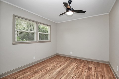 the spacious living room of an empty home with wood flooring and a ceiling fan