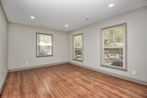 an empty living room with wood flooring and three windows