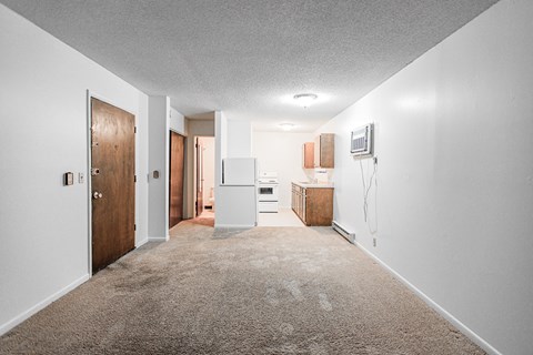 A long hallway with a brown door on the left and a white fridge on the right.