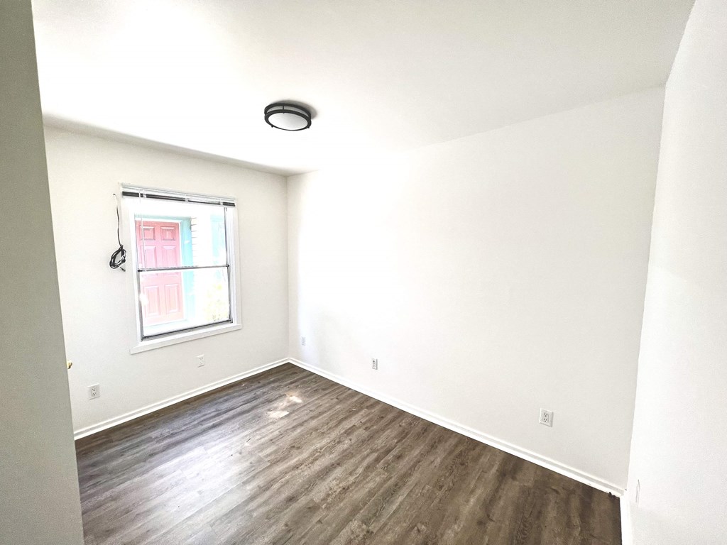 an empty room with white walls and a window and wood floors