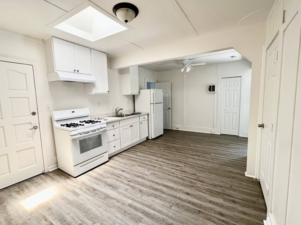 an empty kitchen with white cabinets and appliances and a wood floor