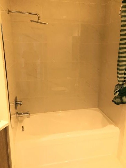 A white bathtub with a shower head and a striped towel hanging on the shower rod.
