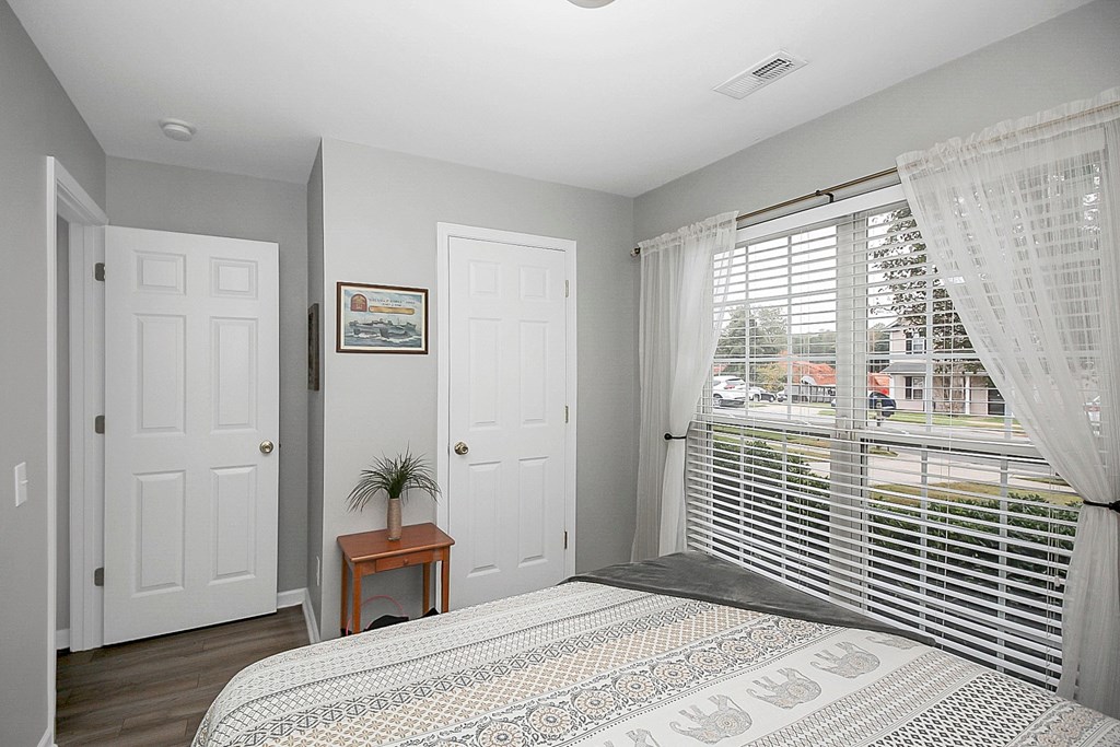 a bedroom with a large window with blinds and a bed