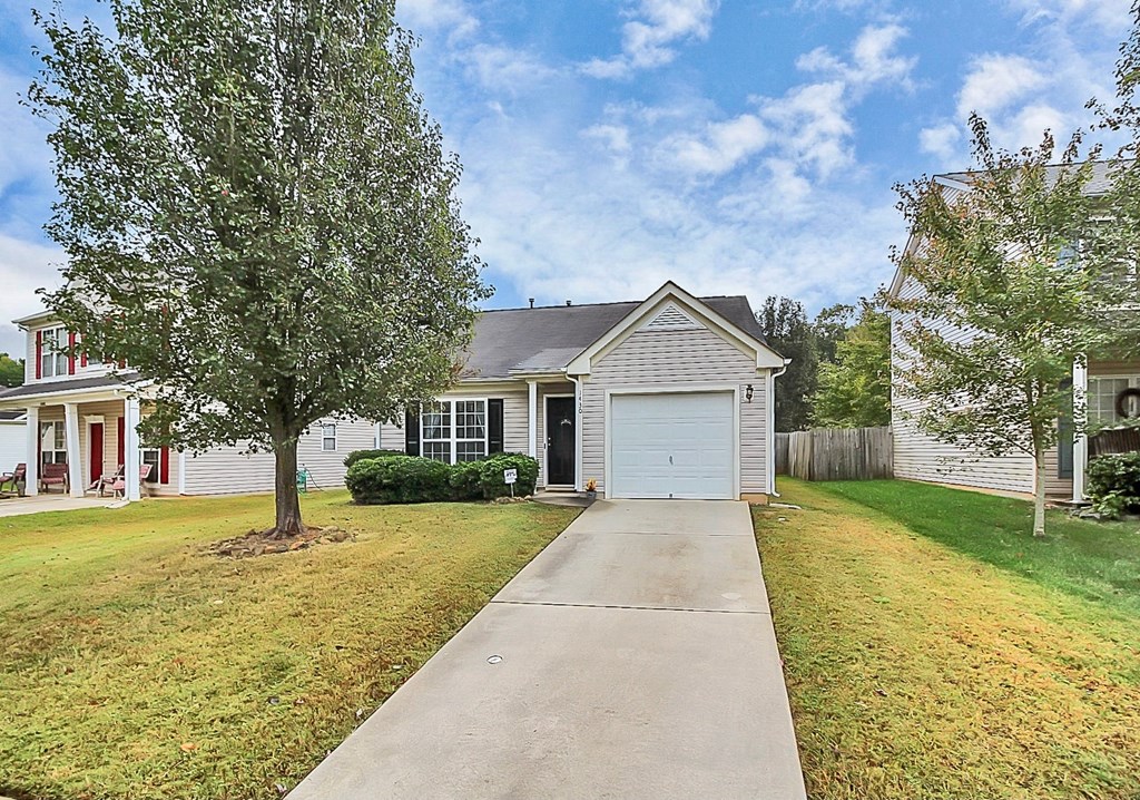 the front of a white house with a driveway and a tree