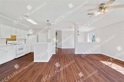 A spacious kitchen with white cabinets and a wooden floor.
