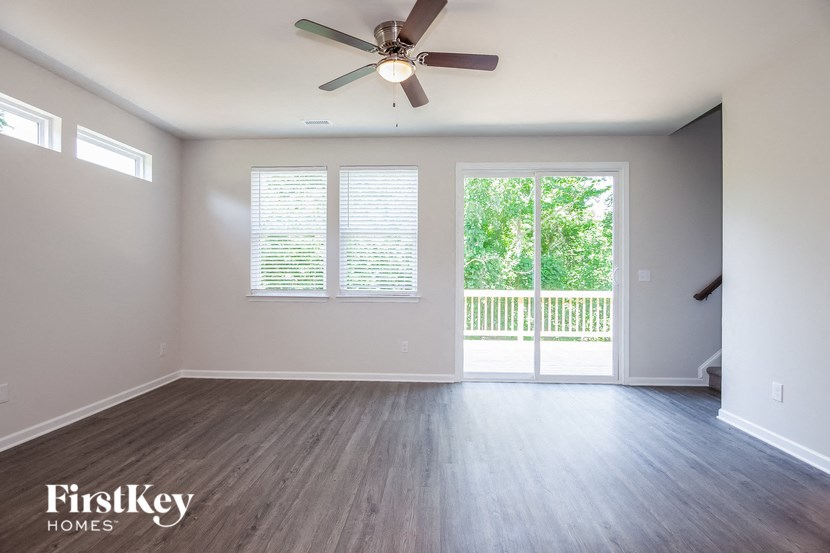 an empty living room with a ceiling fan and a balcony