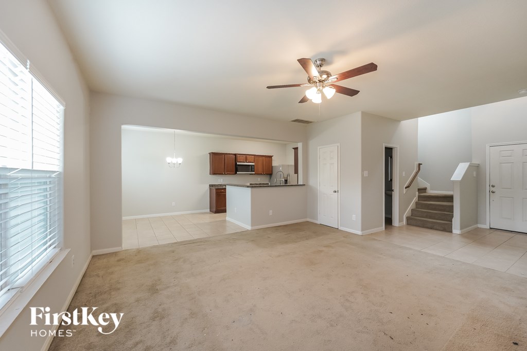 A spacious living room with a ceiling fan and a kitchenette in the background.