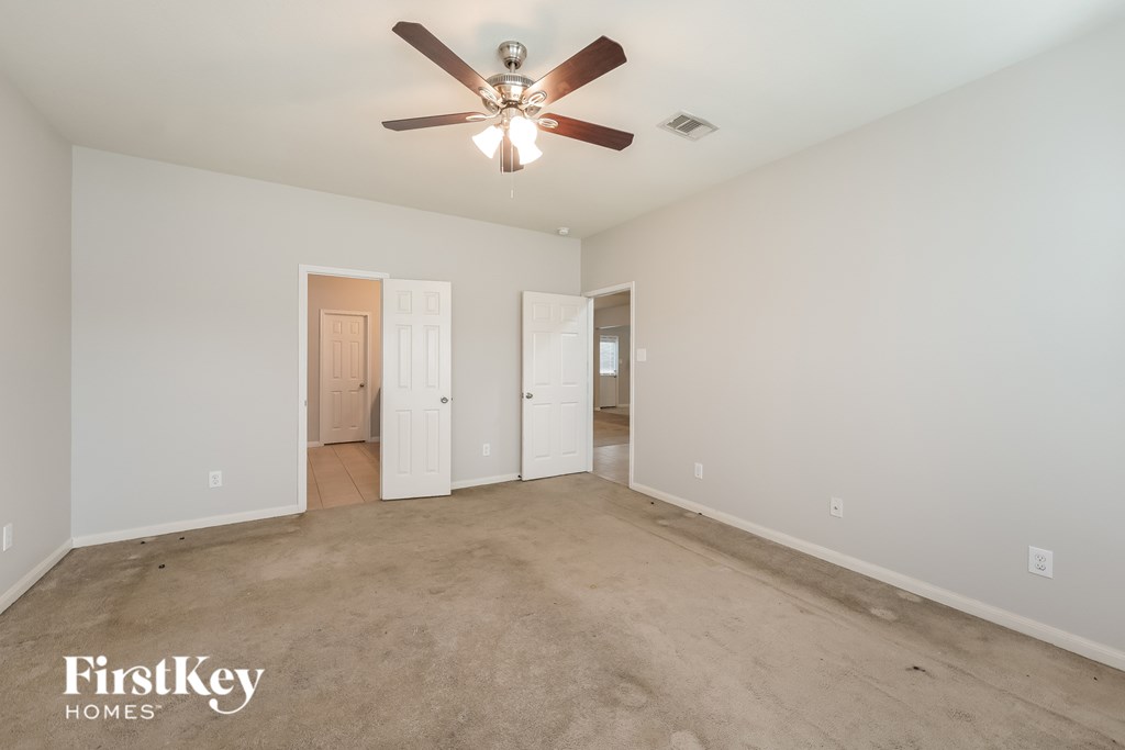 A spacious room with a ceiling fan and three doors.