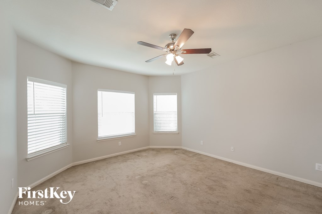 A spacious room with a ceiling fan and three windows.