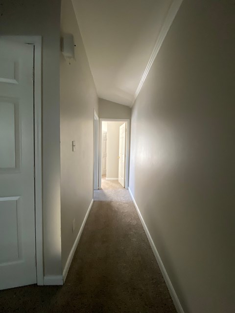 A hallway with a white door on the left and a light at the end.
