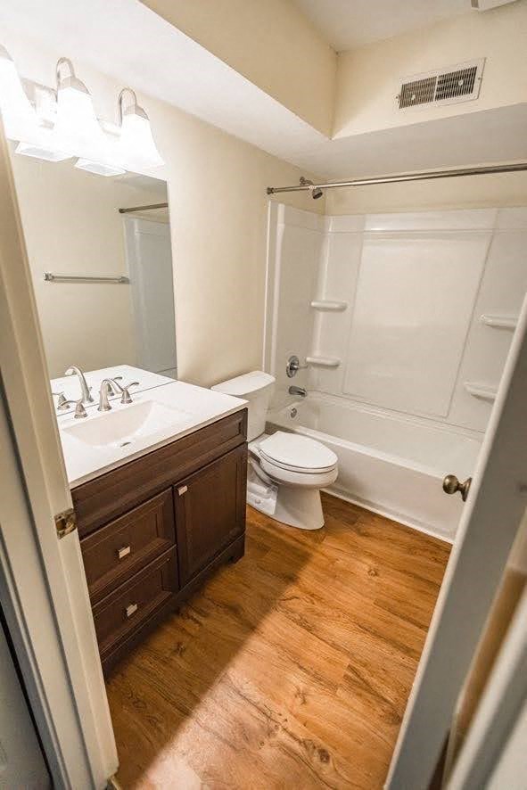 A white toilet sits in a bathroom with wooden floors.