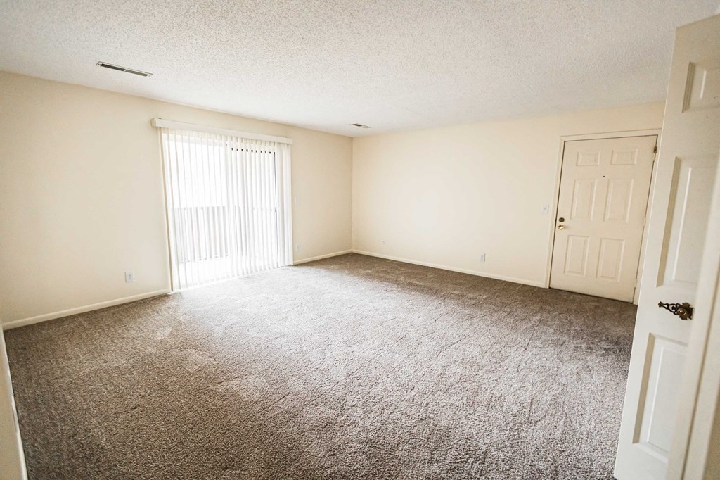 A room with a carpeted floor and a window with blinds.
