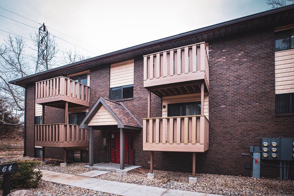 A brick building with a red door and a balcony.