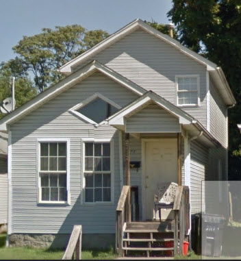 A small house with a grey siding and a white door.
