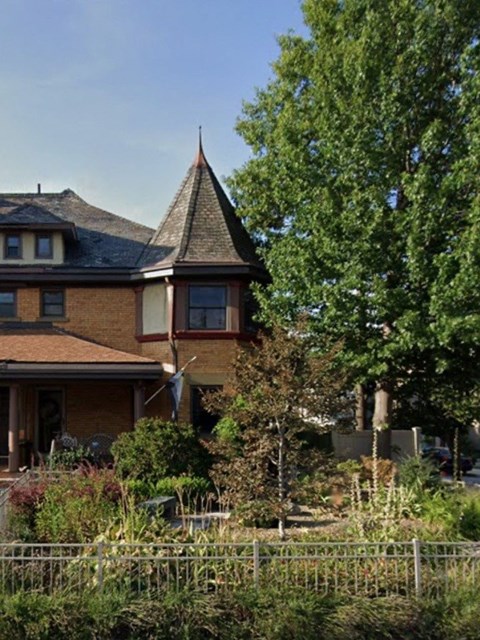 A house with a steeply pitched roof and a tower is surrounded by a garden.