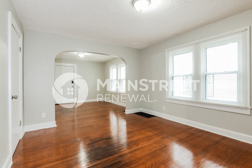a renovated living room with a hard wood floor and two windows