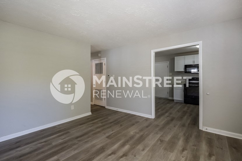 a renovated living room with wood flooring and a door to the kitchen