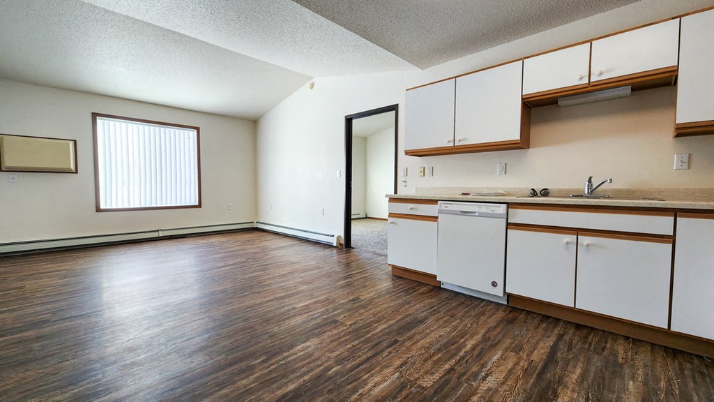 an empty living room and kitchen with wood floors and white cabinets