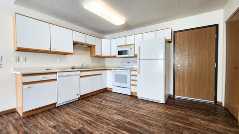 an empty kitchen with white appliances and wood floors