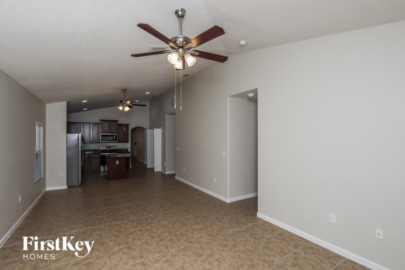 A spacious room with a ceiling fan and a kitchen area in the background.