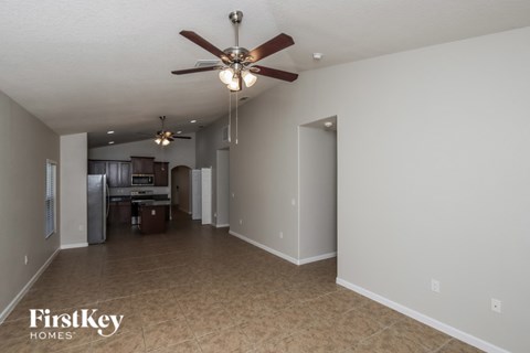 A spacious room with a ceiling fan and a kitchen area in the background.