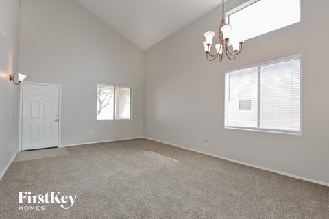 A spacious room with a carpeted floor, a chandelier, and two windows with blinds.