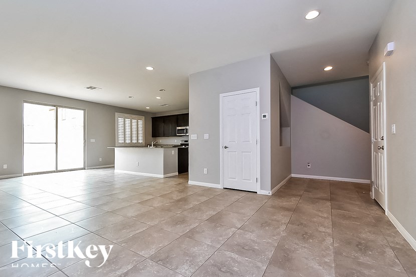 A spacious, empty room with tile flooring and a kitchen area in the background.