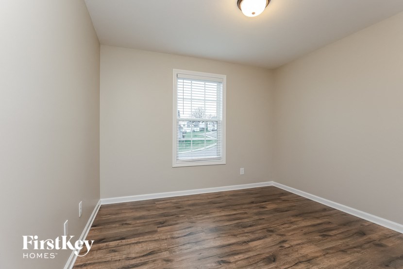 A room with wooden flooring and a window showing a view of a building.